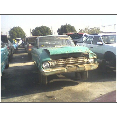 1972 Ford Ranchero - A weathered green vehicle sits in a lot filled with other cars, showing significant front-end damage.