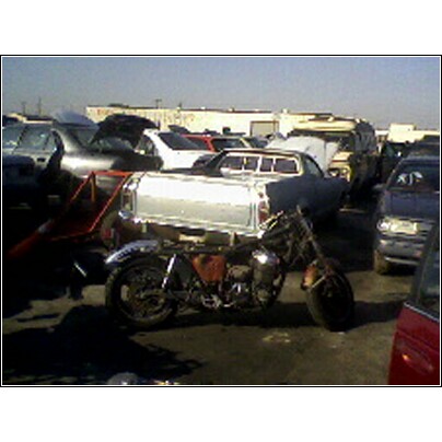 1972 Ford Ranchero - A motorcycle is parked in front of a pickup truck in a junkyard with other vehicles in the background.