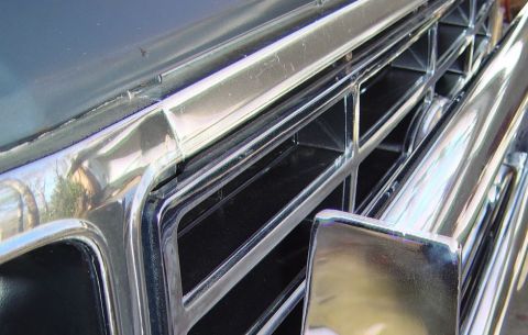 1986 Ford Bronco - Close-up of a vehicle's chrome grille, reflecting the surrounding environment.
