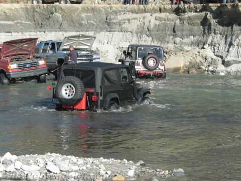 1987 Suzuki Samurai - Multiple off-road vehicles navigate a river crossing on a rocky terrain.