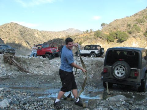 1987 Suzuki Samurai - A group of Jeeps are off-roading in a rocky, muddy terrain, with one person pulling a strap.