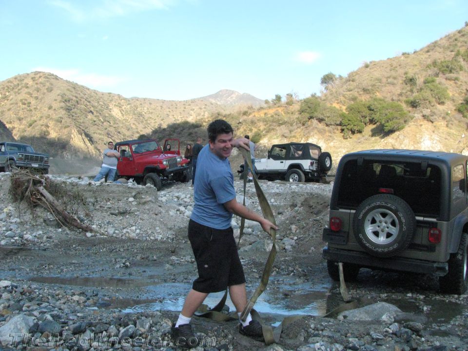 guy pulling a strap attached to a Jeep in a rocky, muddy area with other Jeeps around