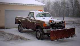 1996 Ford Crown Victoria - A brown pickup truck equipped with a snow plow sits parked in the snow, ready for winter conditions.