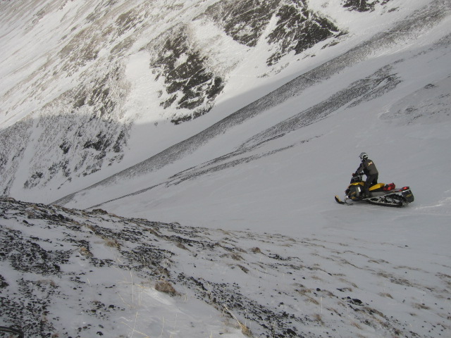 Rider on yellow snowmobile crossing a steep snowy mountain slope