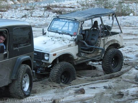 1987 Suzuki Samurai - A white 1987 Suzuki Samurai navigates rough terrain alongside another off-road vehicle.
