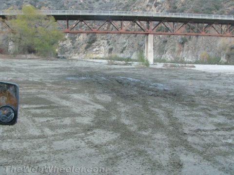 1987 Suzuki Samurai - View from a vehicle's side mirror shows tire tracks in the mud near a bridge.