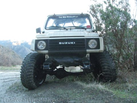 1987 Suzuki Samurai - A modified Suzuki Samurai sits on a dirt road with large off-road tires and a visible roll cage.