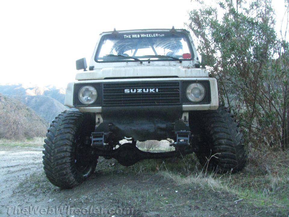 White Suzuki Samurai with large tires and roll cage, parked on dirt road