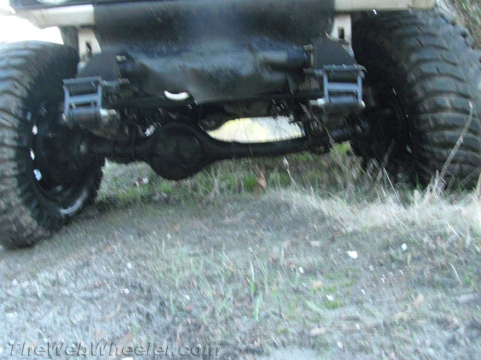 Off-road vehicle rear axle with large tires, showing suspension components and a dark undercarriage