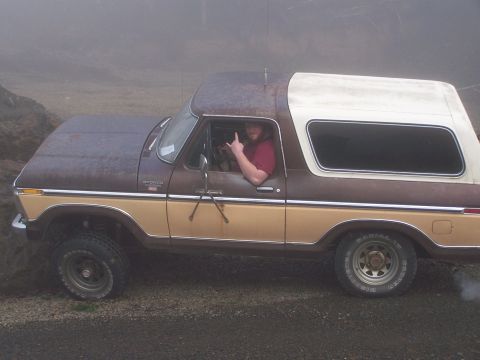 1978 Ford Bronco - A person in a two-tone brown and tan Ford Bronco makes a hand gesture while driving on a dirt road.