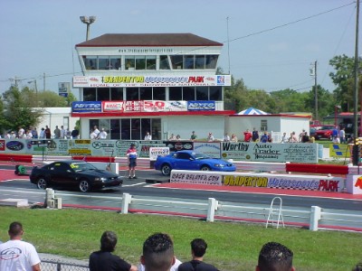 1996 Ford Crown Victoria - A drag race is about to begin with two cars lined up on the track in front of the grandstands and control tower.