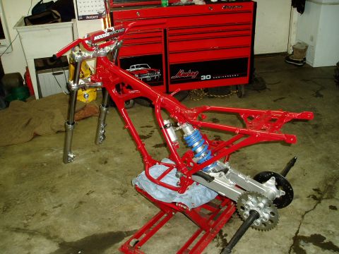 2000 Ford E350 - The red frame of a motorcycle, with a blue shock absorber and suspension components, is shown on a red lift in a garage setting.