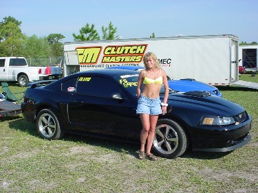 1996 Ford Crown Victoria - Woman poses with a black Ford Mustang in front of a Clutch Masters trailer and other vehicles.
