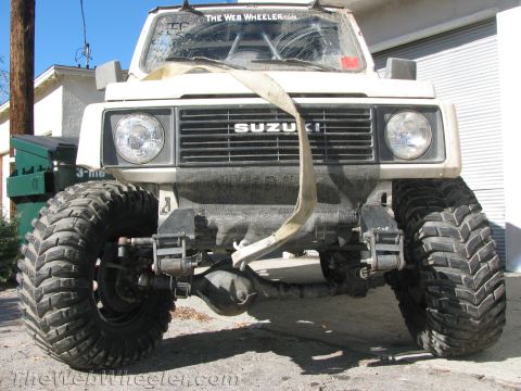 1987 Suzuki Samurai - Front view of a modified 1987 Suzuki Samurai with prominent off-road tires and a tow strap.