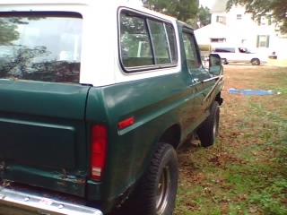 1979 Ford Bronco - The rear of a green 1978 Ford Bronco with a white camper shell is visible, parked in a grassy area.
