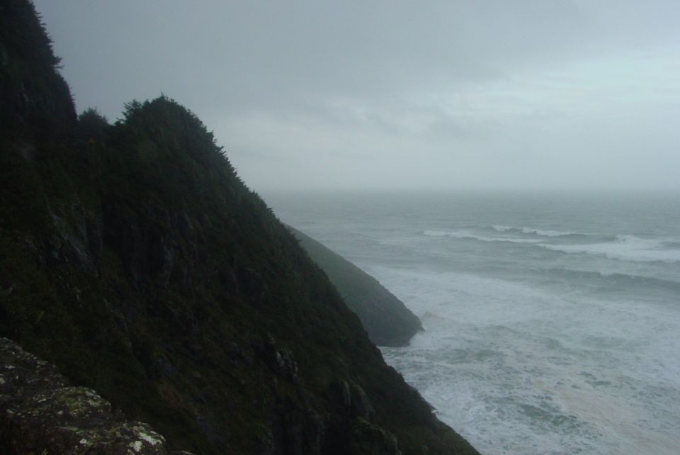 Stormy ocean waves crash against a rocky, tree-covered coastline under an overcast sky. Supermotors.net logo in lower right