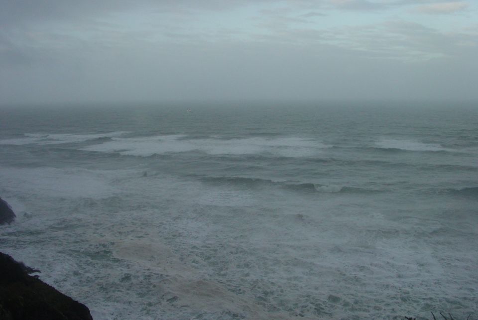 choppy ocean waves under a cloudy sky, with a rocky shore on the left