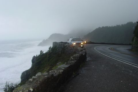 1993 Ford Bronco - Two vehicles drive along a foggy coastal highway with rough seas visible below.