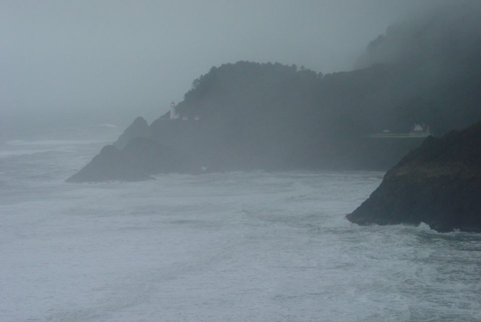 Stormy ocean waves crash against rocky cliffs with a lighthouse visible on the hill