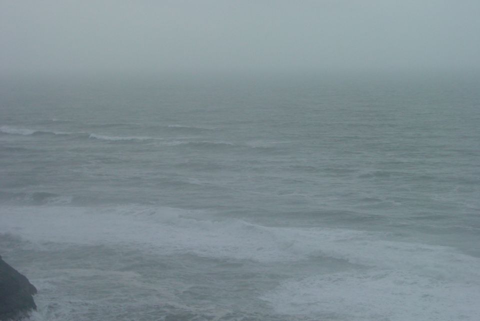 Ocean waves crashing on a rocky shore under a foggy sky. Supermotors logo in the corner