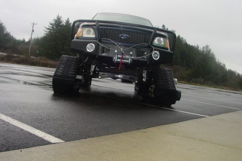 1993 Ford Bronco - A modified Ford truck with tracks instead of wheels is parked on a wet asphalt surface.