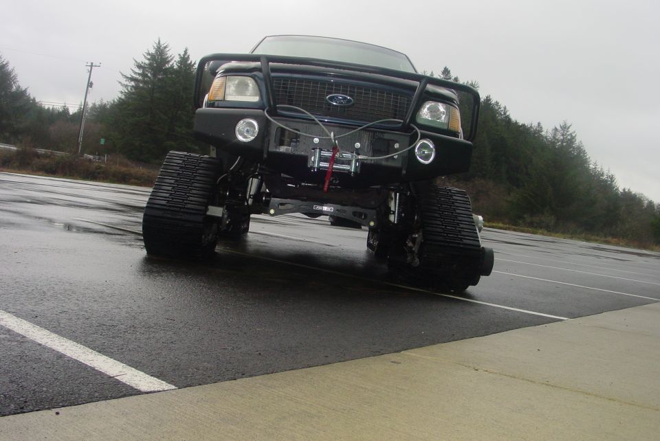 Black Ford truck with tracks, winch, and bull bar, viewed from the front