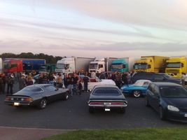 1991 Ford Crown Victoria - A diverse collection of vehicles, including trucks and classic cars, are gathered outdoors under a cloudy sky.