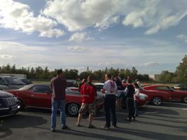1991 Ford Crown Victoria - People gather around classic cars at an outdoor car show event under a cloudy sky.