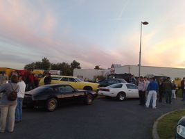 1991 Ford Crown Victoria - A gathering of cars and people are seen outside a building as the sun sets.