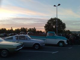 1991 Ford Crown Victoria - A collection of classic vehicles are parked in a lot under a colorful sunset sky.