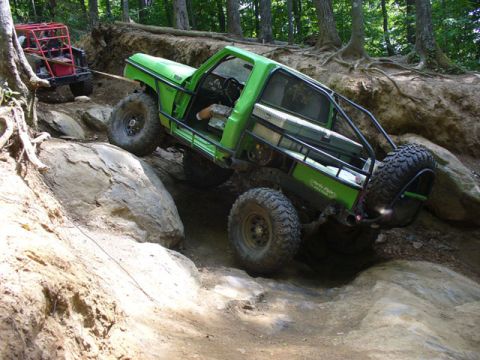 1978 Ford Bronco - Two off-road vehicles navigate a challenging rocky trail in a wooded area.
