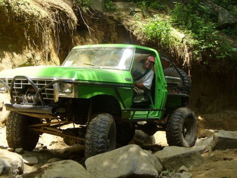 1978 Ford Bronco - A modified green SUV tackles a challenging rocky trail with a driver visible inside.