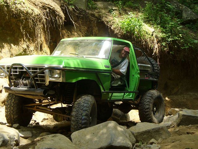 Green off-road SUV with a winch and large tires navigating rocky terrain
