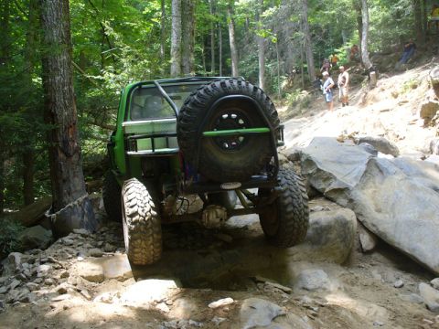 1978 Ford Bronco - This modified off-road vehicle is carefully maneuvering over large rocks on a steep, wooded trail.