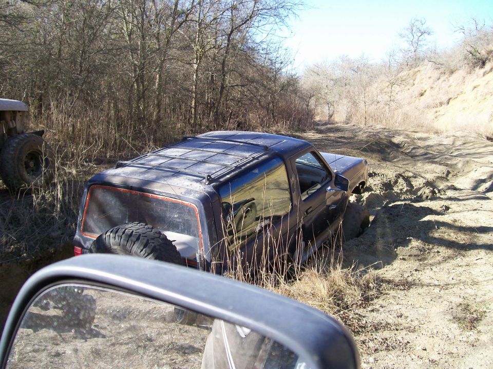 Black two-door Ford Bronco stuck at an angle in a muddy off-road trail