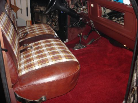 1979 Ford F-150 - The interior of a 1979 Ford F-150 shows plaid bench seats, red carpeting, and a disassembled dashboard.