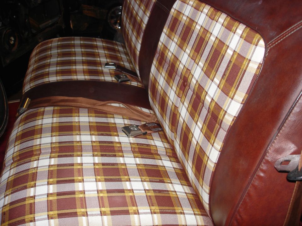Close-up of a plaid bench seat with brown leather trim and seatbelts