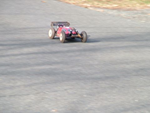 1994 Ford Bronco - A red remote control buggy with white wheels is captured in motion on an asphalt surface.