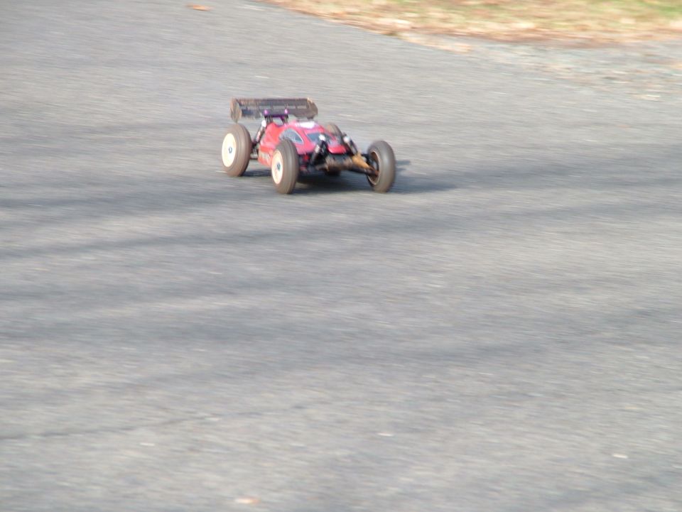 Red remote control buggy with white wheels driving on asphalt