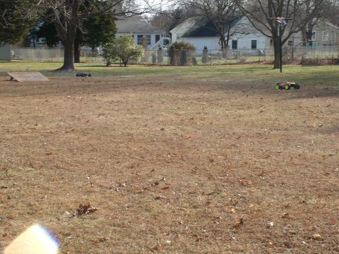 1994 Ford Bronco - Two remote control cars are visible on a dry grass field with houses in the distance.