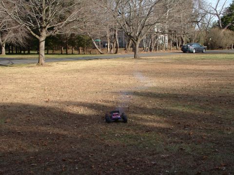 1994 Ford Bronco - A remote control monster truck is shown on a grassy field with a car driving on a road in the distance.