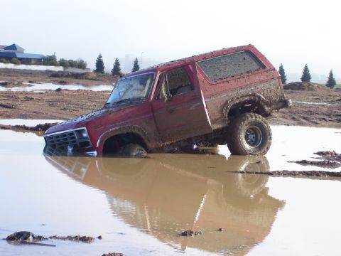 1986 Ford Bronco - This red Ford Bronco is stuck in a muddy puddle, with its front end submerged.