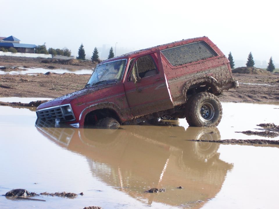 Red Ford Bronco stuck deep in mud, front wheels submerged
