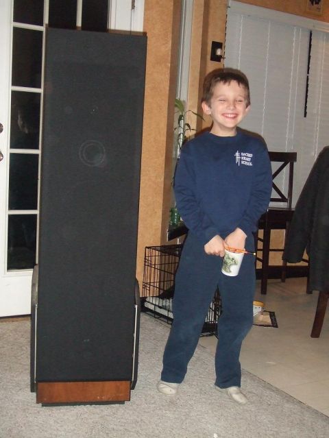 1987 Ford Bronco - A young boy smiles while holding a cup, standing beside a large speaker in an indoor setting.
