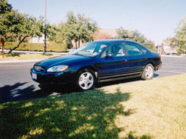Dark blue 2000-2003 Ford Taurus sedan parked on grass beside a parking lot