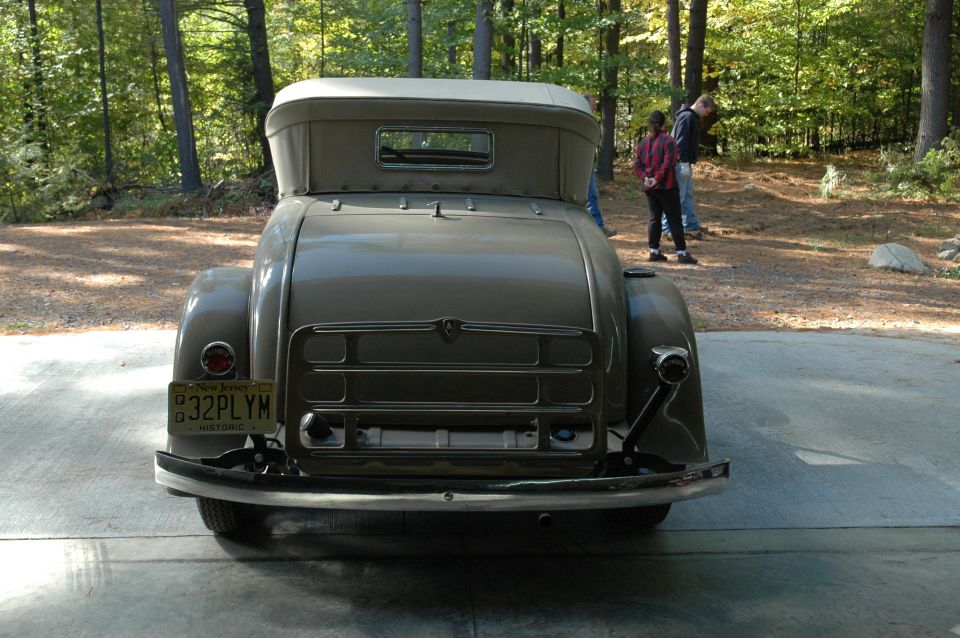 Rear of olive vintage convertible with NJ '32PLYM' historic plate, parked in woods