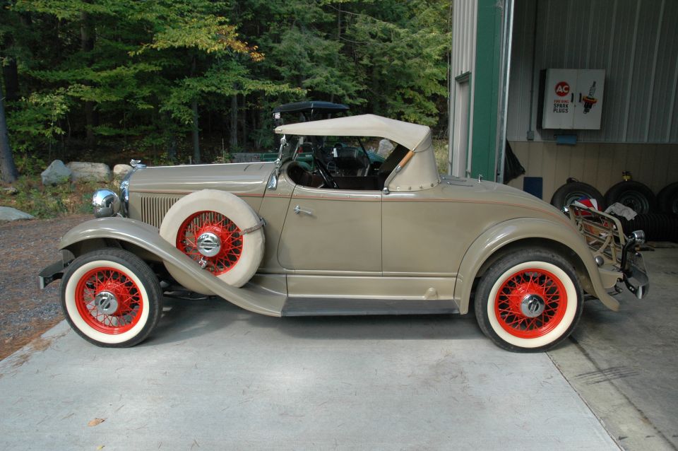 Tan vintage roadster, side view, red wire wheels, whitewalls, parked by garage