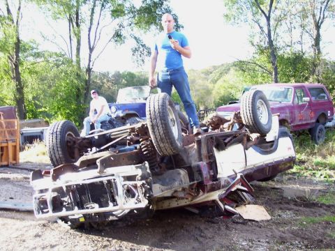 1979 Ford Pickup - An overturned vehicle chassis is the main focus, with two men and other vehicles in the background.