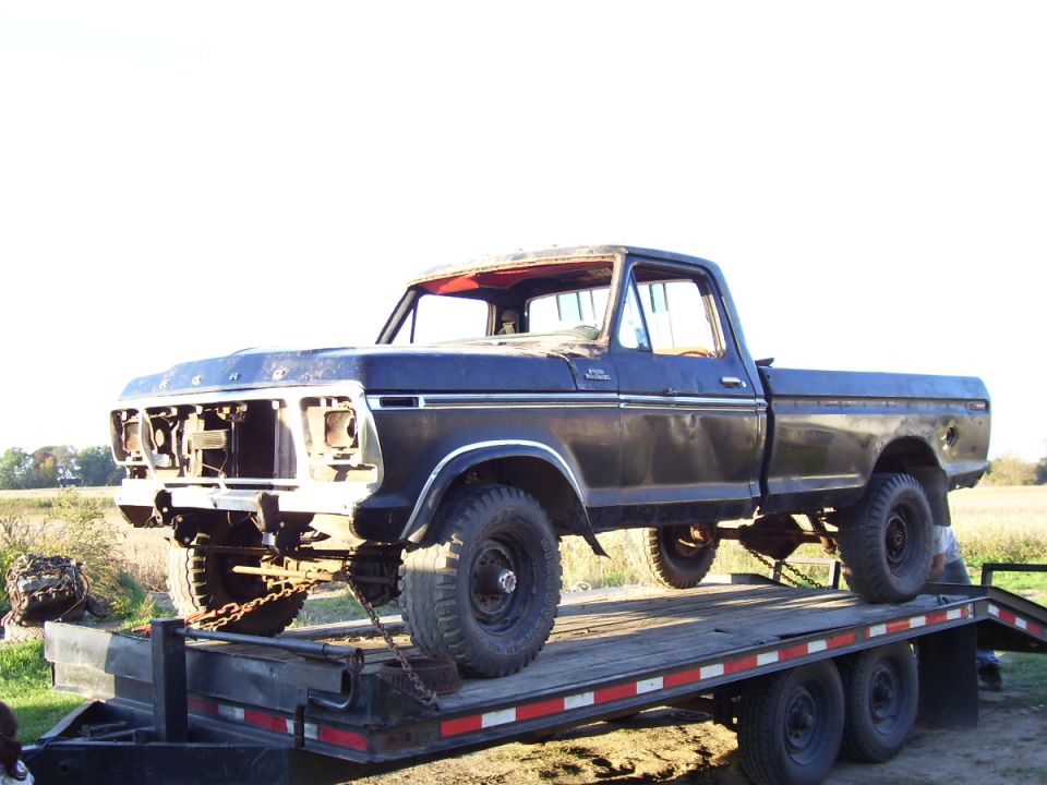 Dark blue 1979 Ford pickup truck on a flatbed trailer, front grille missing, some rust visible