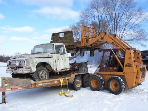 1979 Ford Pickup - A white pickup truck is being loaded onto a trailer by a yellow skid steer loader in a snowy environment.